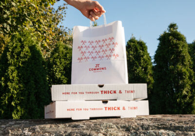 Two pizza boxes with hand holding takeout bag outside